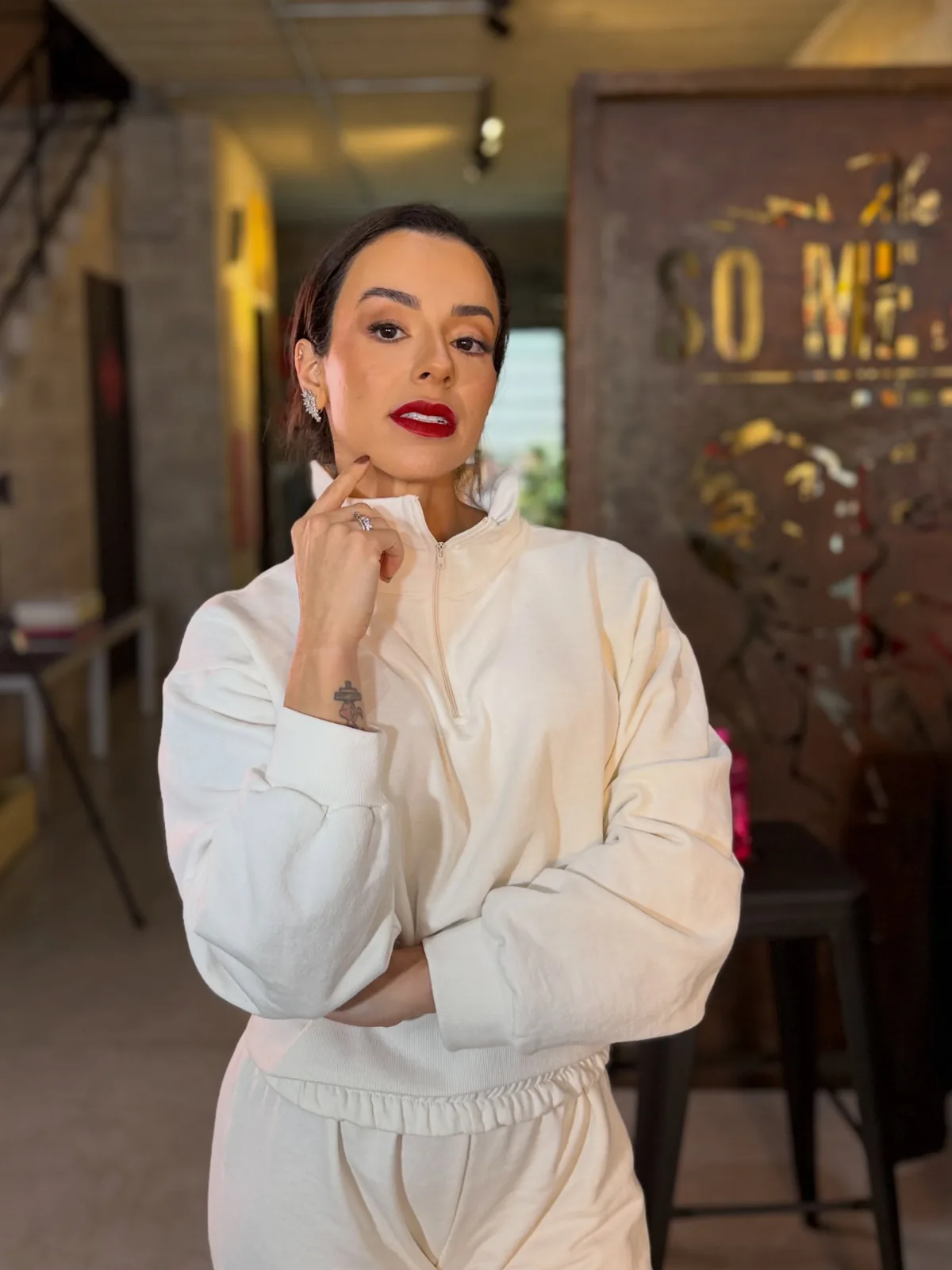 Larissa Melo de conjunto branco, com a mão no queixo, num restaurante
